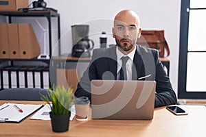 Middle age bald man working at the office thinking attitude and sober expression looking self confident