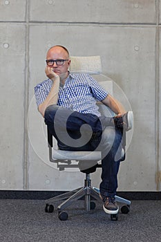 Middle age balding man with eyeglasses bad sitting position on chair in office