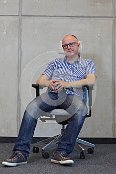 Middle age balding man with eyeglasses bad sitting position on chair in office