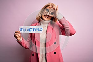 Middle age beautiful blonde business woman holding paper with you are fired message with happy face smiling doing ok sign with