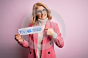 Middle age beautiful blonde business woman holding paper with you are fired message with surprise face pointing finger to himself