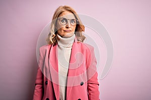 Middle age beautiful blonde business woman wearing elegant pink jacket and glasses with serious expression on face