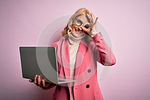 Middle age beautiful blonde business woman working using laptop over pink background with happy face smiling doing ok sign with