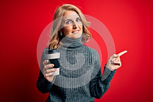 Middle age beautiful blonde woman drinking takeaway cup of coffee over red background very happy pointing with hand and finger to