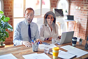 Middle age beautiful business workers working together using laptop at the office afraid and shocked with surprise expression,