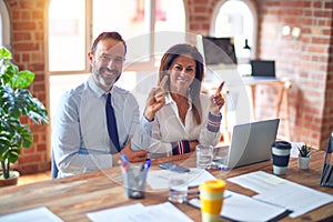 Middle age beautiful business workers working together using laptop at the office with a big smile on face, pointing with hand and