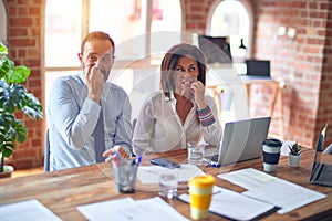 Middle age beautiful business workers working together using laptop at the office looking stressed and nervous with hands on mouth