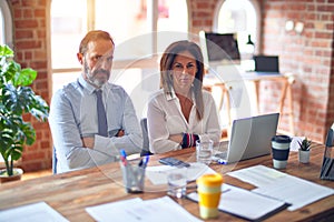 Middle age beautiful business workers working together using laptop at the office skeptic and nervous, disapproving expression on