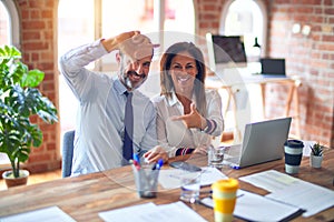 Middle age beautiful business workers working together using laptop at the office smiling making frame with hands and fingers with