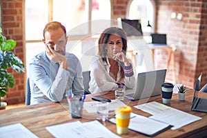 Middle age beautiful business workers working together using laptop at the office thinking looking tired and bored with depression