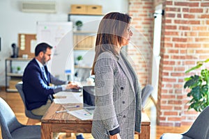 Middle age beautiful businesswoman wearing jacket and glasses standing at the office looking to side, relax profile pose with