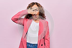 Middle age beautiful businesswoman wearing jacket standing over isolated pink background peeking in shock covering face and eyes