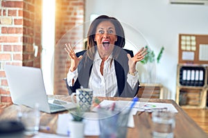 Middle age beautiful businesswoman working using laptop at the office celebrating crazy and amazed for success with arms raised