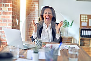 Middle age beautiful businesswoman working using laptop at the office celebrating mad and crazy for success with arms raised and