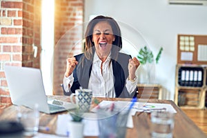 Middle age beautiful businesswoman working using laptop at the office celebrating surprised and amazed for success with arms