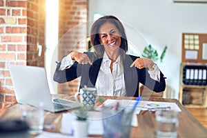 Middle age beautiful businesswoman working using laptop at the office looking confident with smile on face, pointing oneself with