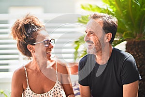 Middle age beautiful couple sitting on terrace speaking and smiling