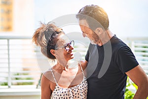 Middle age beautiful couple standing on terrace speaking and smiling