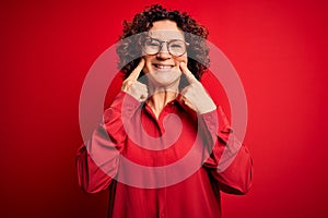 Middle age beautiful curly hair woman wearing casual shirt and glasses over red background Smiling with open mouth, fingers