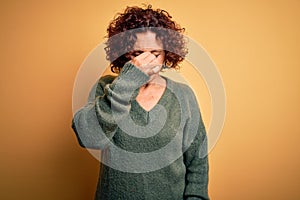 Middle age beautiful curly hair woman wearing casual sweater over  yellow background tired rubbing nose and eyes feeling