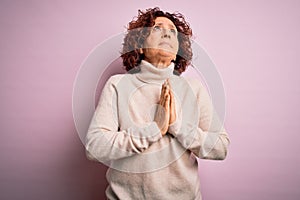 Middle age beautiful curly hair woman wearing casual turtleneck sweater over pink background begging and praying with hands