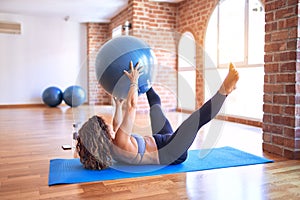 Middle age beautiful sportswoman doing exercise using fitness ball in a class of yoga at gym