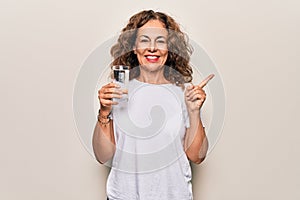 Middle age beautiful woman drinking glass of water to refreshment over white background smiling happy pointing with hand and