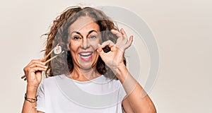 Middle age beautiful  woman eating sushi using wooden chopsticks over white background doing ok sign with fingers, smiling