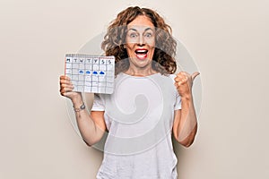 Middle age beautiful woman holding climatology calendar showing cloudy and rainy weather pointing thumb up to the side smiling photo