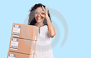 Middle age beautiful woman holding delivery package smiling happy doing ok sign with hand on eye looking through fingers