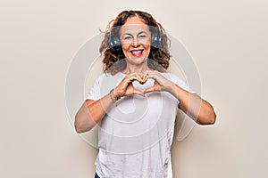 Middle age beautiful woman listening to music using headphones over white background smiling in love doing heart symbol shape with