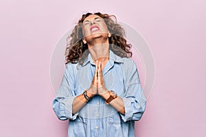 Middle age beautiful woman wearing casual denim shirt standing over pink background begging and praying with hands together with