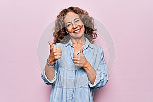 Middle age beautiful woman wearing casual denim shirt standing over pink background Pointing to the back behind with hand and