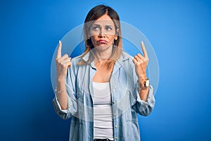 Middle age beautiful woman wearing casual shirt standing over isolated blue background Pointing up looking sad and upset,
