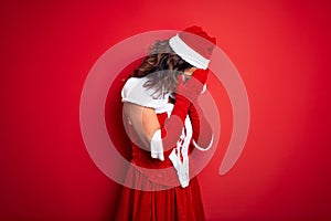 Middle age beautiful woman wearing Santa Claus costume over isolated red background with sad expression covering face with hands
