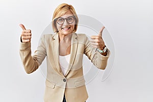 Middle age blonde business woman standing over isolated background success sign doing positive gesture with hand, thumbs up