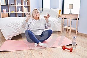 Middle age blonde woman doing yoga exercise at bedroom