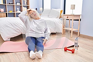Middle age blonde woman smiling confident stretching at bedroom
