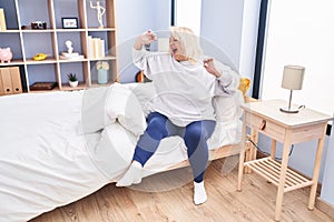 Middle age blonde woman waking up stretching arms at bedroom