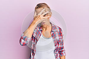 Middle age blonde woman wearing casual clothes and glasses peeking in shock covering face and eyes with hand, looking through