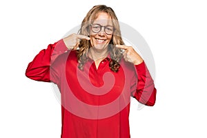 Middle age blonde woman wearing casual shirt over red background smiling cheerful showing and pointing with fingers teeth and