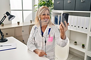 Middle age blonde woman wearing doctor uniform having medical teleconsultation at clinic