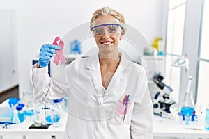 Middle age blonde woman working at laboratory looking for breast cancer cure looking positive and happy standing and smiling with