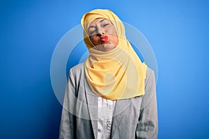 Middle age brunette business woman wearing muslim traditional hijab over blue background looking at the camera blowing a kiss on