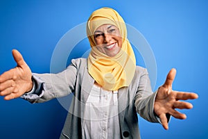 Middle age brunette business woman wearing muslim traditional hijab over blue background looking at the camera smiling with open
