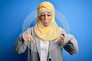 Middle age brunette business woman wearing muslim traditional hijab over blue background Pointing down with fingers showing