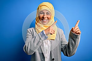 Middle age brunette business woman wearing muslim traditional hijab over blue background smiling and looking at the camera