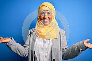 Middle age brunette business woman wearing muslim traditional hijab over blue background smiling showing both hands open palms,