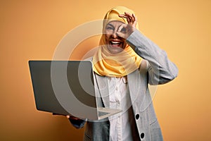 Middle age brunette business woman wearing traditional muslim hijab using laptop with happy face smiling doing ok sign with hand