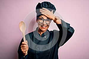 Middle age brunette chef woman wearing cooker uniform and hat holding wooden spoon stressed with hand on head, shocked with shame
